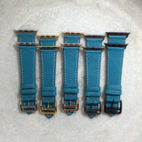 Cyan Blue Apple Watch Band by Juxli Home.  Handmade, stylish leather strap with rose gold hardware on a 40mm Apple watch on a canvas with a black and gray painting.