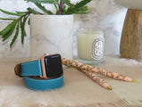 Cyan Blue Double Wrap Apple Watch Leather Band by Juxli Home.  Handmade, stylish leather strap with rose gold hardware on a 40mm Apple watch on a canvas with a black and gray painting.