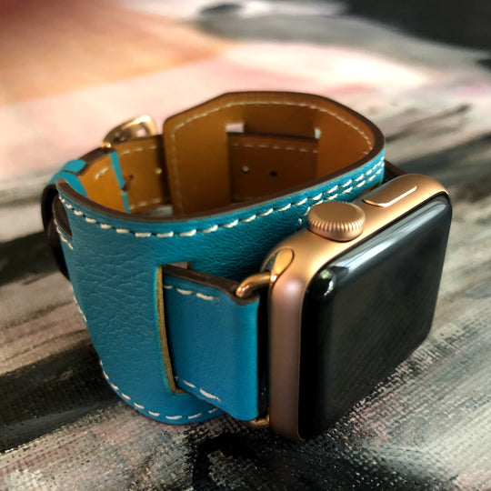 Cyan Blue Apple Watch Leather Cuff by Juxli Home.  Handmade, stylish leather strap with rose gold hardware on a 40mm Apple watch on a canvas with a black and gray painting.