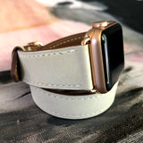 Women’s Ivory Double Wrap Apple Watch Leather Band by Juxli Home.  Handmade, stylish leather strap with rose gold hardware on a 40mm Apple watch on a canvas with a black and gray painting.