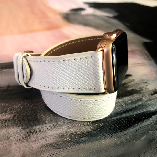 White Double Wrap Textured Leather Apple Watch Band by Juxli Home.  Handmade, stylish leather strap with rose gold hardware on a 40mm Apple watch on a canvas with a black and gray painting.