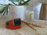 Ladies Fire Orange Double Wrap Apple Watch Leather Band by Juxli Home.  Handmade, stylish leather strap with rose gold hardware on a 40mm Apple watch on a canvas with a black and gray painting.