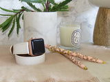 White Double Wrap Textured Leather Apple Watch Band by Juxli Home.  Handmade, stylish leather strap with rose gold hardware on a 40mm Apple watch on a canvas with a black and gray painting.