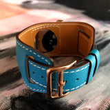 Cyan Blue Apple Watch Leather Cuff by Juxli Home.  Handmade, stylish leather strap with rose gold hardware on a 40mm Apple watch on a canvas with a black and gray painting.