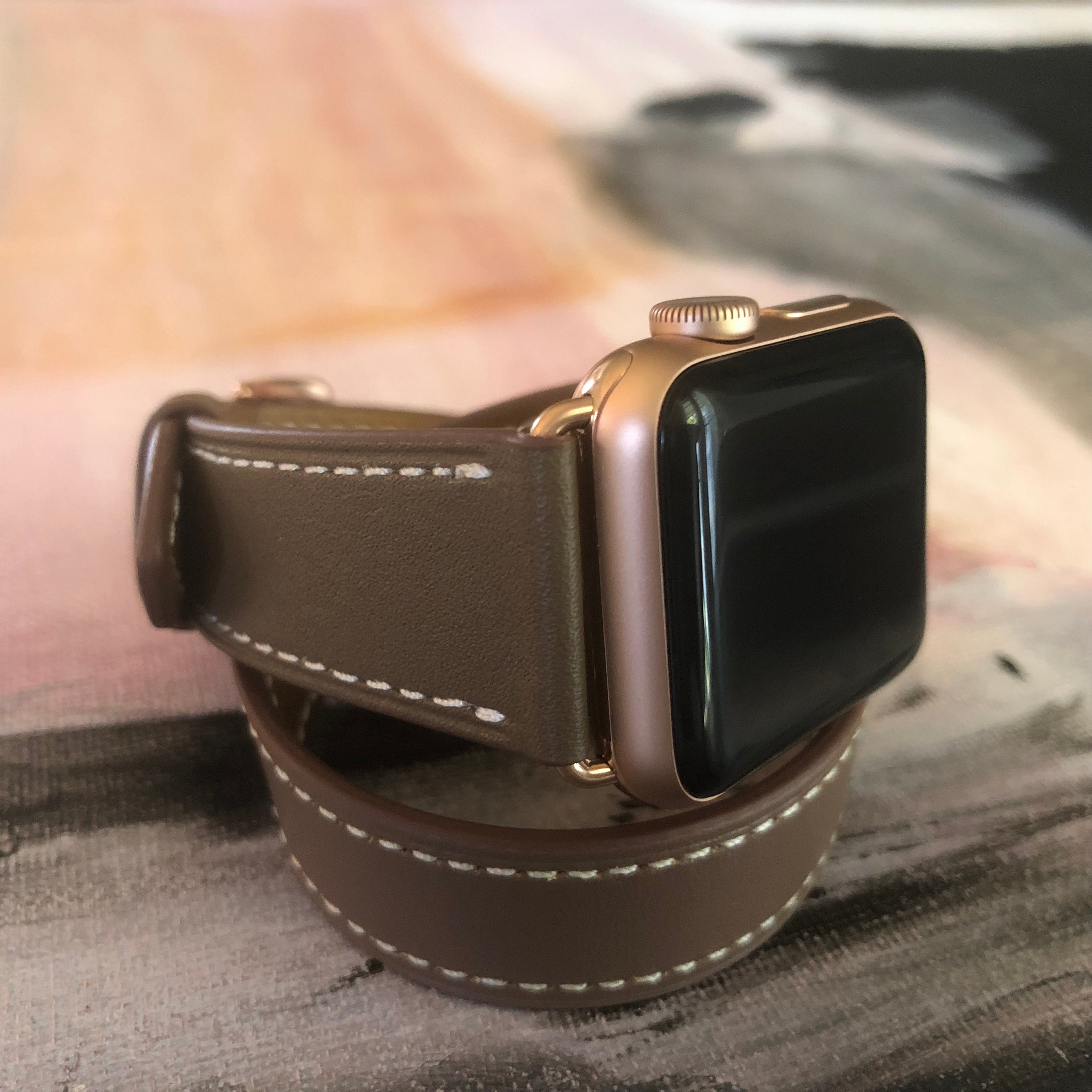 Hazel Brown Double Wrap Apple Watch Leather Band by Juxli Home.  Handmade, stylish leather strap with rose gold hardware on a 40mm Apple watch on a canvas with a black and gray painting.