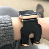 Black Double Buckle Apple Watch Leather Cuff by Juxli Home.  Handmade, stylish leather strap with rose gold hardware on a 40mm Apple watch on a canvas with a black and gray painting.