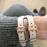 Ivory Apple Watch Double Buckle Cuff by Juxli Home.  Handmade, stylish leather strap with rose gold hardware on a 40mm Apple watch on a canvas with a black and gray painting.