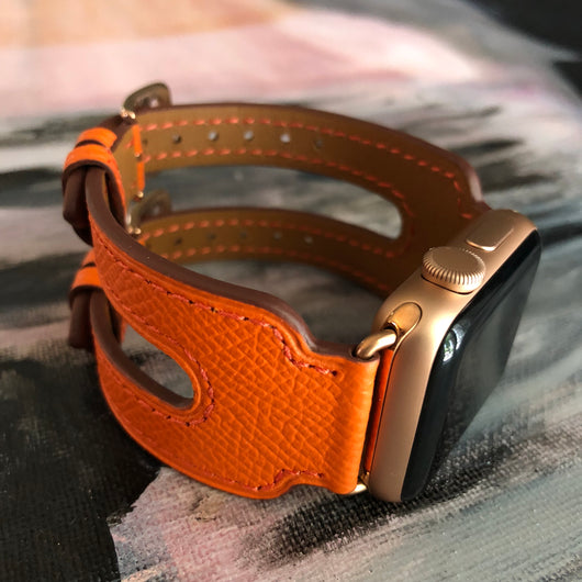 Summer Orange Double Buckle Apple Watch Leather Cuff by Juxli Home.  Handmade, stylish leather strap with rose gold hardware on a 40mm Apple watch on a canvas with a black and gray painting.