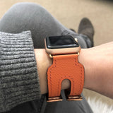 Summer Orange Double Buckle Apple Watch Leather Cuff by Juxli Home.  Handmade, stylish leather strap with rose gold hardware on a 40mm Apple watch on a canvas with a black and gray painting.